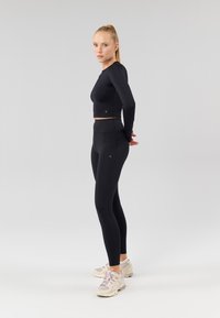 Zwart lange mouwen crop top en hoge taille leggings. Gladde textuur, aansluitend ontwerp. Draag met lichtgekleurde sportschoenen.