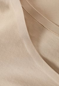 Tissu beige au toucher lisse, présentant un léger éclat et un motif de tricot fin, tombant en douceur avec une finition bordée nette.