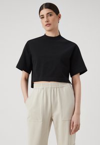 Svart crop-top med korte ermer og høy hals, parret med lysebeige høyt liv bukser med store lommer.