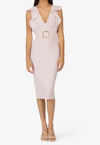 Robe ajustée longueur genoux en rose clair, avec des manches à volants et un décolleté en V profond, maintenue par une boucle carrée dorée à la taille.