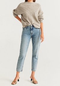 Hellgrauer gestrickter Pullover mit Zickzackmuster, kombiniert mit hochtaillierten blauen Jeans und schwarzen Riemchen-Absatzsandalen.