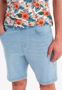 Shorts en denim bleu clair avec une coupe décontractée, dotés de poches latérales et d'une taille élastiquée avec cordon de serrage. Le tissu a une texture douce et une couture classique.