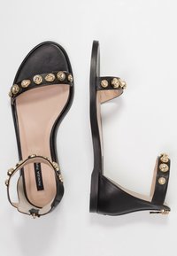 Sandali in pelle nera con dettagli in oro e cristallo, design con punta aperta e cinturino alla caviglia con chiusura a zip sul retro.