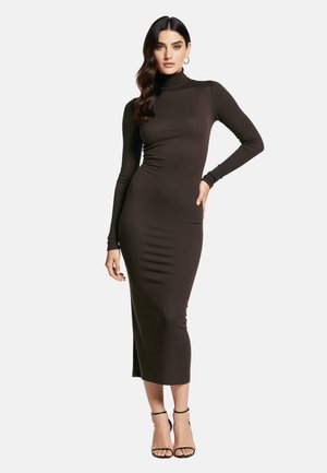 Brązowa prążkowana sukienka o długości midi z długim rękawem, wysokim kołnierzem i bocznym rozcięciem, zestawiona z czarnymi sandałkami na paski i kolczykami kołami. Gładka faktura.