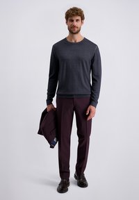 Donkergrijze lange mouwen trui met ronde hals, gecombineerd met kastanjebruine broeken. De persoon houdt een donker colbert vast en draagt donkere schoenen.