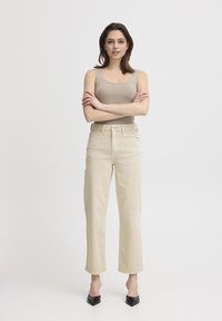 Jeans beige a vita alta con taglio dritto, orli risvoltati e chiusura con bottone metallico. Abbinati a un top aderente beige e tacchi neri.
