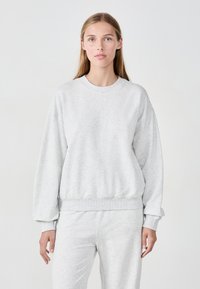 Hellgrauer Sweatshirt mit Rundhalsausschnitt, langen Ärmeln und gerippten Bündchen sowie Saum, aus weichem, strukturiertem Stoff gefertigt. Kombiniert mit passenden Hosen.