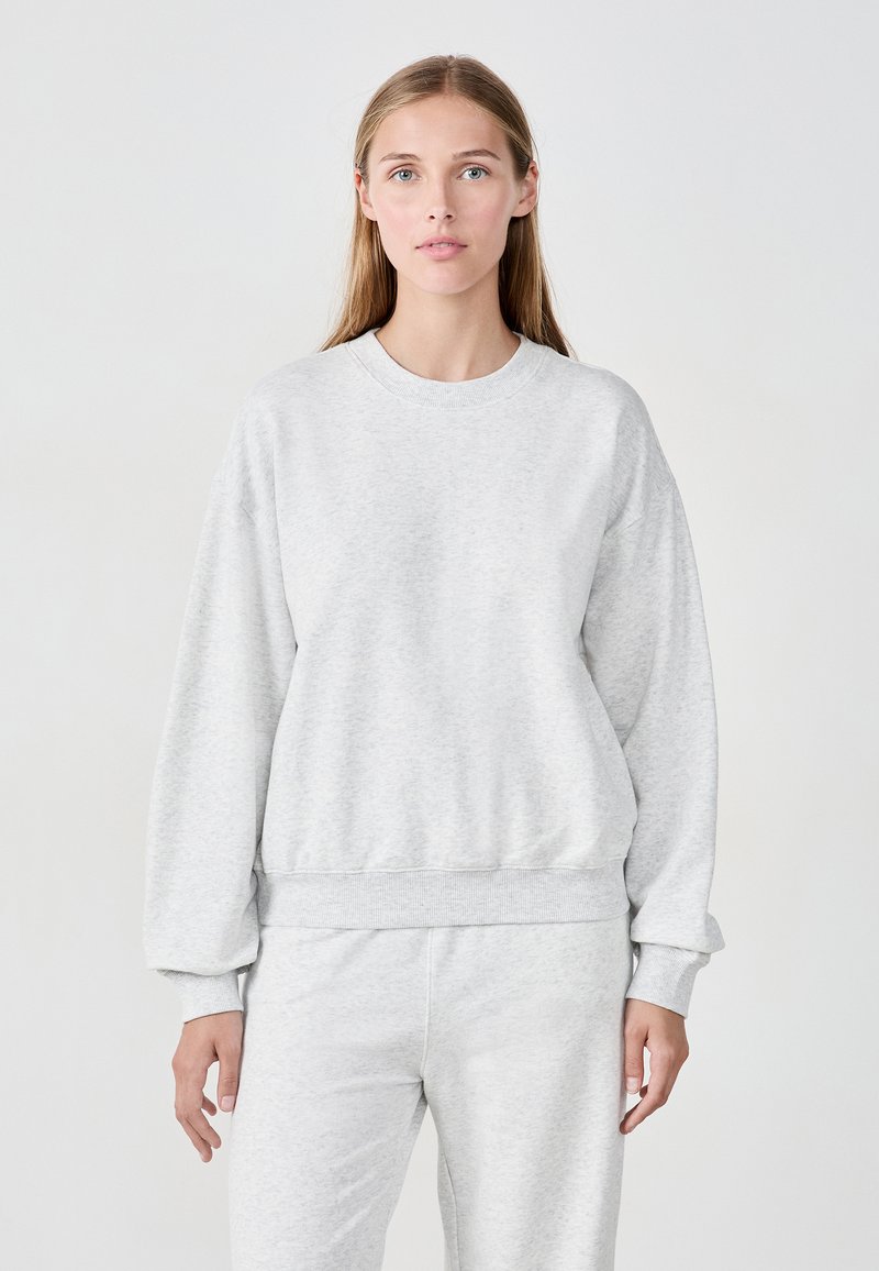 Hellgrauer Sweatshirt mit Rundhalsausschnitt, langen Ärmeln und gerippten Bündchen sowie Saum, aus weichem, strukturiertem Stoff gefertigt. Kombiniert mit passenden Hosen.