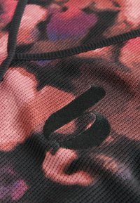 Textured fabric with a pink and black floral pattern. Features a prominent black logo, round neckline, and contrasting black seams.