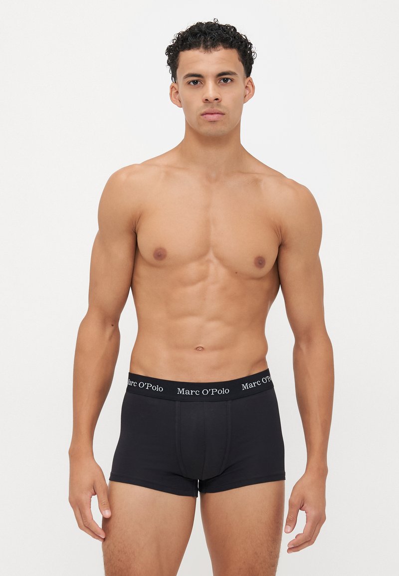 Schwarze Boxershorts mit einem weichen, elastischen Bund, der den Text "Marc O'Polo" in Weiß trägt. Glattes Material, taillierte Passform und eine Länge bis zur Mitte des Oberschenkels.
