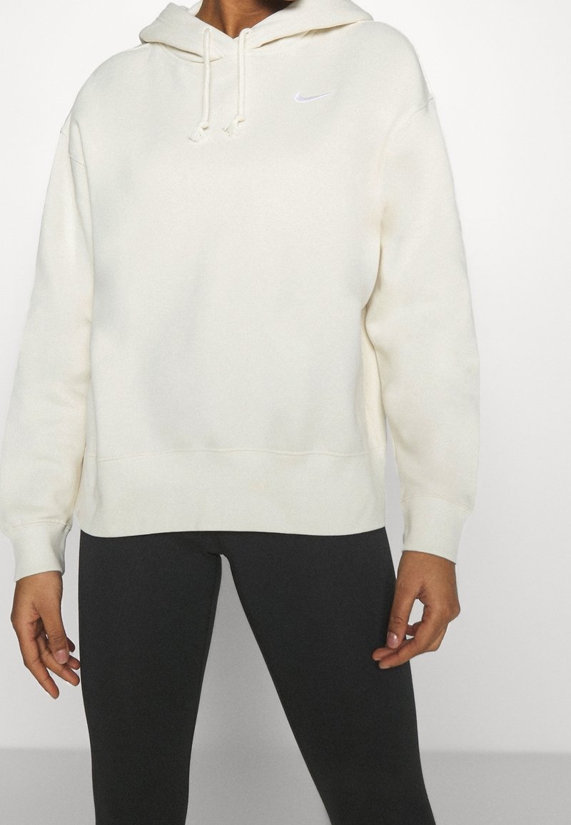 Bílá fleece mikina s kapucí, přední kapsou a stahovacími šňůrkami, s malým šedým logem Nike na hrudi a žebrovanými manžetami.
