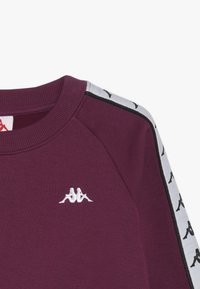 Sudadera burdeos con cuello redondo acanalado, que presenta un logotipo bordado blanco y rayas laterales en plata y negro con patrón.