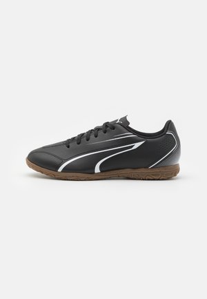 Baskets de sport noires avec un dessus synthétique lisse, des accents blancs, un design à lacets et une semelle en caoutchouc texturée.