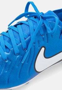 Sininen urheilukenki, jossa on teksturoitu päällinen, nauhakiristys, valkoinen Nike-logo ja musta yksityiskohta pohjan varrella. Sileä materiaali, jossa on voimakkaat ompeleet.