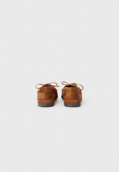 Scarpe in suede marrone con una texture liscia, punta rotonda e lacci a fiocco. Presentano una suola a profilo basso e un accento sul tallone posteriore per una maggiore stabilità.