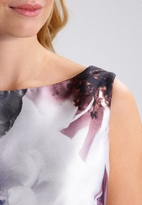 Femme portant une robe sans manches avec un motif floral abstrait violet, noir et blanc, dévoilant l'épaule ainsi qu'une partie du cou et du visage.