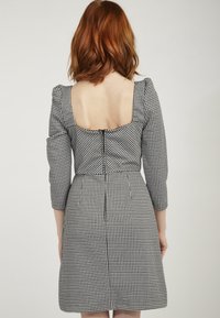 Czarna i biała sukienka w jodełkę z rękawami do łokcia z bufkami i kwadratowym dekoltem z tyłu. Posiada dopasowany gorset i rozkloszowaną spódnicę.