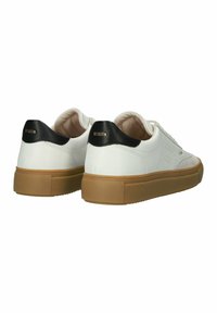 Sneaker in pelle bianca con accentuazione nera sul tallone, punta rotonda e suola in gomma beige con superficie texturizzata; branding minimale sul tallone.