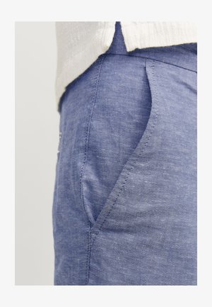 Blue linen pants with a textured finish, featuring a side pocket and a tailored fit, partially visible beneath a white garment.