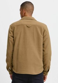 Tan fleece jack met een kraag, een lusdetail aan de achterkant en knoopsluitingen bij de mouwen. Glad textuur, relaxte pasvorm, geen zichtbare logo's of patronen.