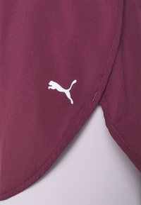 Vinsjorts-mössa i vinröd färg med en strömlinjeformad design, mjuk textur, rundad fåll och en vit Puma-logotyp på nedre vänstra sidan.