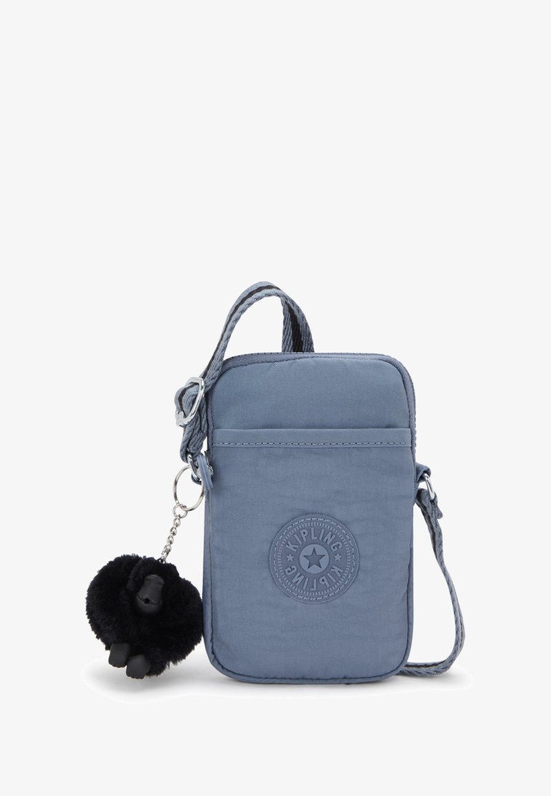 Piccola borsa a tracolla blu con tracolla regolabile, tasca frontale, patch con logo Kipling e un portachiavi a forma di scimmia di peluche nero attaccato.