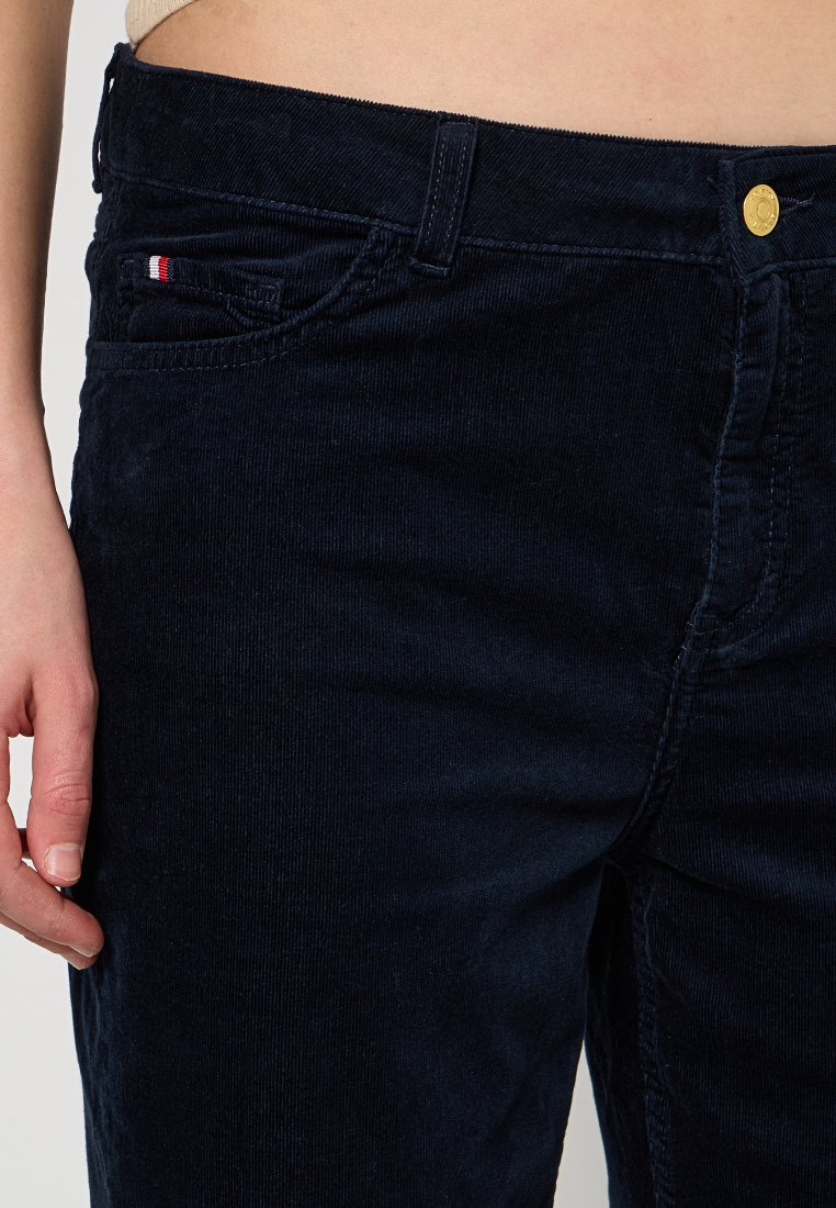 Marinefarbene Cordhosen mit strukturiertem Finish. Merkmale sind eine Vordertasche mit rot-weißen Details und einem goldenen Knopfverschluss.