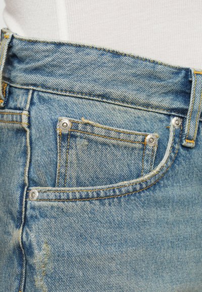 Lys blå denimbukser med høy midje, kontrasterende gule sømmer, en liten frontlomme og sølvfargede detaljer.