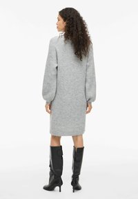 Graues gestricktes Kleid mit langen Ärmeln, lockerer Passform und einem Saum bis zu den Knien, kombiniert mit hohen schwarzen Stiefeln mit Absatz.