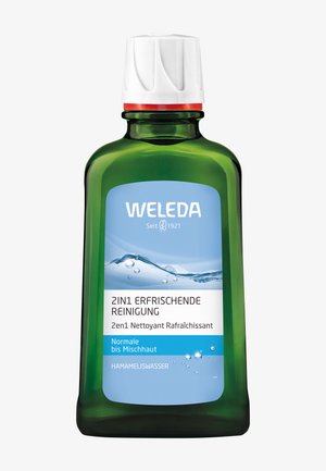 Groene glazen fles met een witte dop en rode accenten. Het etiket heeft blauwe en witte tekst, die aangeeft dat het een 2-in-1 verfrissende reiniger is met hamameliswater.