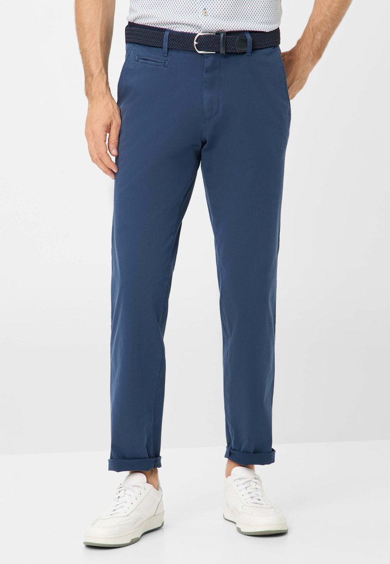 Pantalon en coton bleu avec une coupe slim, ourlets retroussés et une ceinture texturée de couleur foncée, associé à des baskets blanches. Comprend des poches latérales.