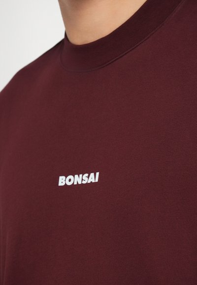 Bordo kokvilnas T-krekls ar apļa kaklu un baltu "BONSAI" tekstu uz priekša. Gluda tekstūra, vienkāršs dizains un īsas piedurknes.