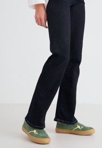 Vaqueros negros de pierna recta con detalles de costura sutil, combinados con zapatillas de ante verde que tienen un acento rosa y suela de goma.
