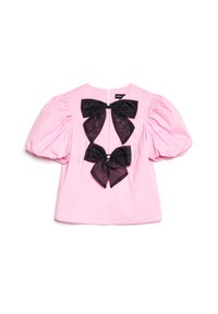 Růžová blůza s krátkým rukávem, balónkovými rukávy a dvěma velkými černými mašlemi uprostřed přední části, z nichž každá má malý dekorativní kámen.