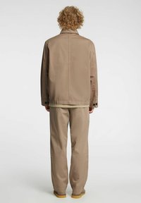 Beige jakke med rett passform og krage, kombinert med matchende bukser med løs passform. Begge plagg har en glatt tekstur og minimalt med detaljer.