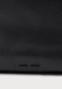 Sac en cuir noir avec une texture lisse, arborant le logo embossé "Samsøe Samsøe". Design minimaliste avec une forme rectangulaire.