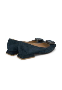 Ballerine in suede blu navy con tacco quadrato basso. Presentano due grandi pietre decorative nere nella parte anteriore. Texture morbida e design della punta arrotondata.