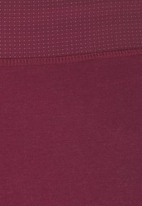 Vinröda leggings med ett slätt, elastiskt tyg. Den övre delen har ett prickigt mönster och är sammanfogad med en sydd söm.