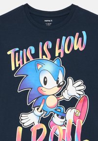 Granatowy bawełniany T-shirt z kolorową grafiką postaci z niebieskimi kolcami, różowymi butami oraz napisem "THIS IS HOW I ROLL" w pogrubionych literach.