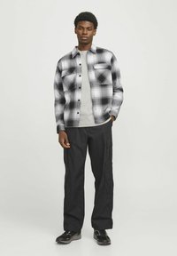 Sort og hvid ternet skjorte med knapper og to brystlommer, båret over en grå t-shirt, parret med sorte cargo bukser og mørke sneakers.