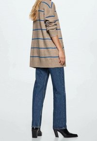 Beżowy sweter w paski z niebieskimi liniami, luźny fason, ściągacze na rękawach, zestawiony z prostymi niebieskimi dżinsami i czarnymi botkami na obcasie.