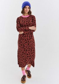 Šaty s leopardím potiskem v hnědé barvě s růžovým límečkem. Dlouhé rukávy, midi délka a postranní rozparky. Nosené s růžovými ponožkami a hnědými teniskami.