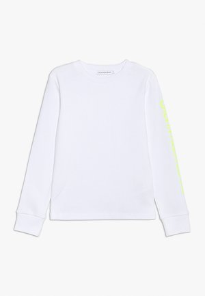 Hvid langærmet crewneck-trøje med Calvin Klein Jeans-mærke på kraven og subtil gul tekst trykt vertikalt på højre ærme.