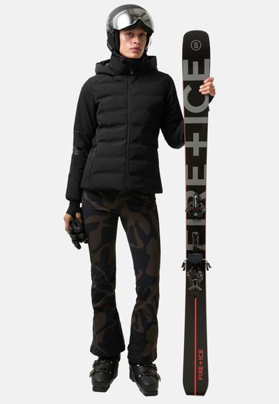 Zwarte pufferjas met zakken met rits, patroonbroek in donkere tinten, handschoenen, helm en ski met bindingen, met het label "FIRE + ICE."