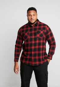 Rode en zwarte geruite flanellen shirt met lange mouwen, knoopsluiting en twee borstzakken. Textuurstof met een gecheckt patroon.