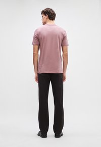 Tielko s krátkymi rukávmi, svetlofialovej farby, s okrúhlym výstrihom, v kombinácii s čiernymi voľnými nohavicami a čiernymi topánkami, zobrazené zozadu.