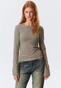 Lange mouwen gestreepte top in beige en donkerbruin, met een ronde hals en uitlopende mouwen, gecombineerd met blauwe spijkerbroek.