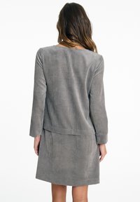 Graues Cordkleid mit langen Ärmeln, einem runden Ausschnitt und einem leicht ausgestellt geschnittenen Saum. Verfügt über eine vertikale Rippstruktur im gesamten Kleid.