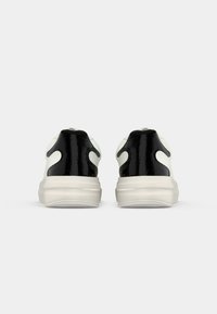 Schwarz-weiße Sneaker mit einer glatten, glänzenden schwarzen Ferse und einem strukturierten weißen Obermaterial. Dicke Sohle mit einem grauen Akzent.