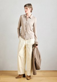 Bežina košulja dugih rukava s ovratnikom, dugmadi sprijeda; uparen s širokim bijelim hlačama. Smeđi kaput prebačen preko jednog ramena. Smeđe čizme na petu.